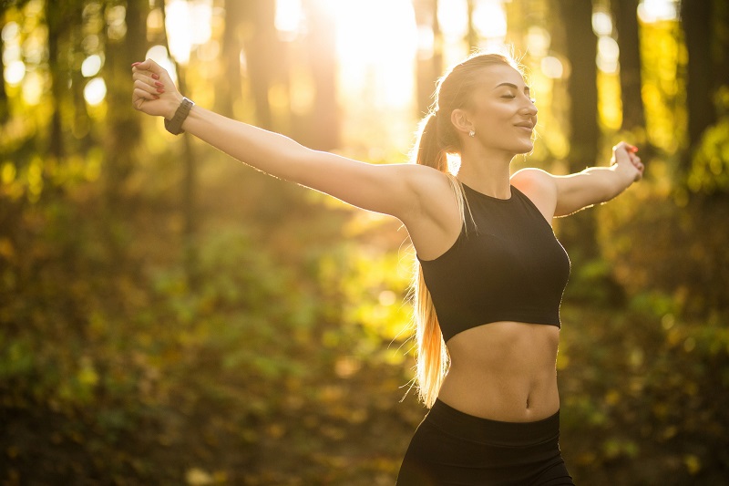 Basics of CBD Woman in Workout Clothes in a Forest with Her Arms Stretched Out to the Sides