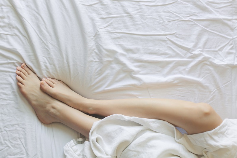 CBD Oil for Sleep Overhead View of a Woman's Legs Partly Covered with Blankets on a Bed
