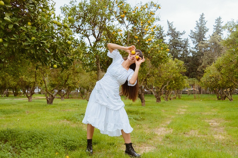Full Spectrum CBD Products Woman in an Orange Grove Holding Two Oranges in Front of Her Face in a Joking and Playful Manner