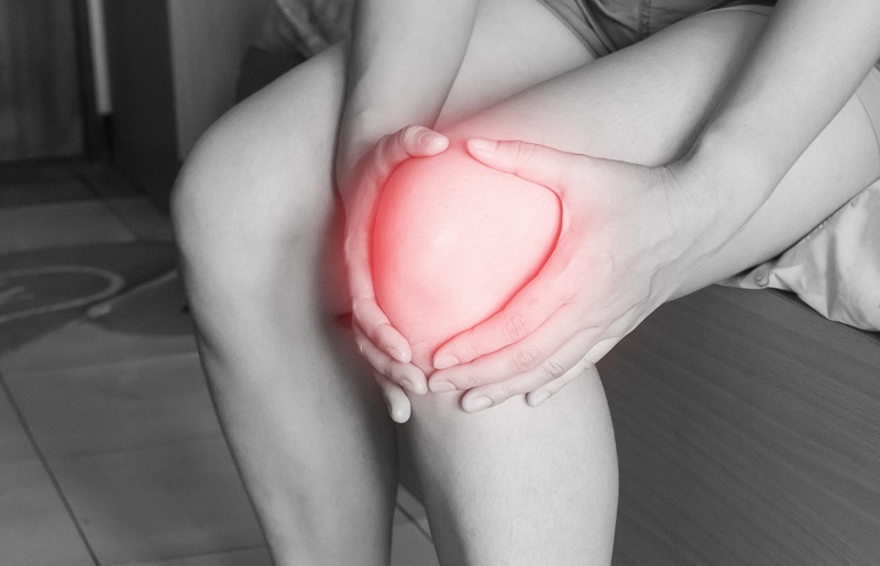 How to Use CBD for Inflammation Black and White Photo of a Woman's Knee with Red Light Around it as She Holds it