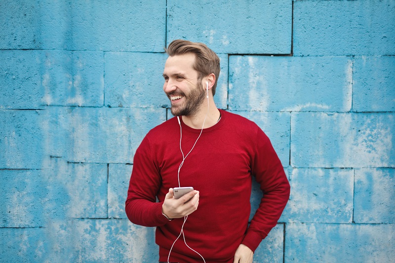 How to Use CBD for Inflammation a Man Standing Against a Blue Brick Wall with Earbuds in His Ears