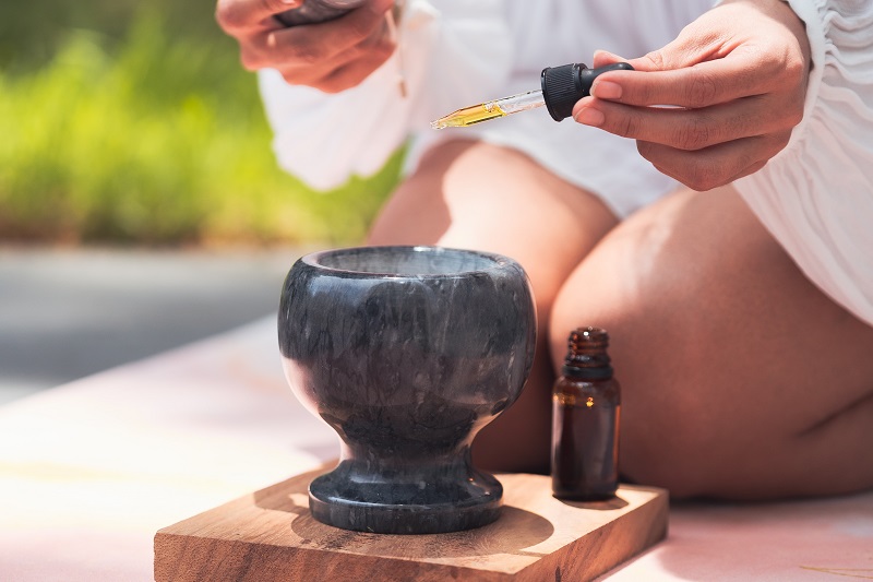 PlantMD Uses GMP Standards Close Up of a Woman Kneeling Down Using a Dropper to Add CBD Oil into a Diffuser