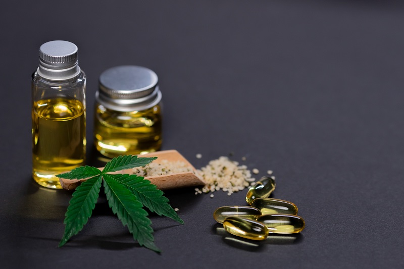 PlantMD Uses GMP Standards Close Up of a Cannabis Plant Leaf with CBD Oil in Tiny Jars and Capsules