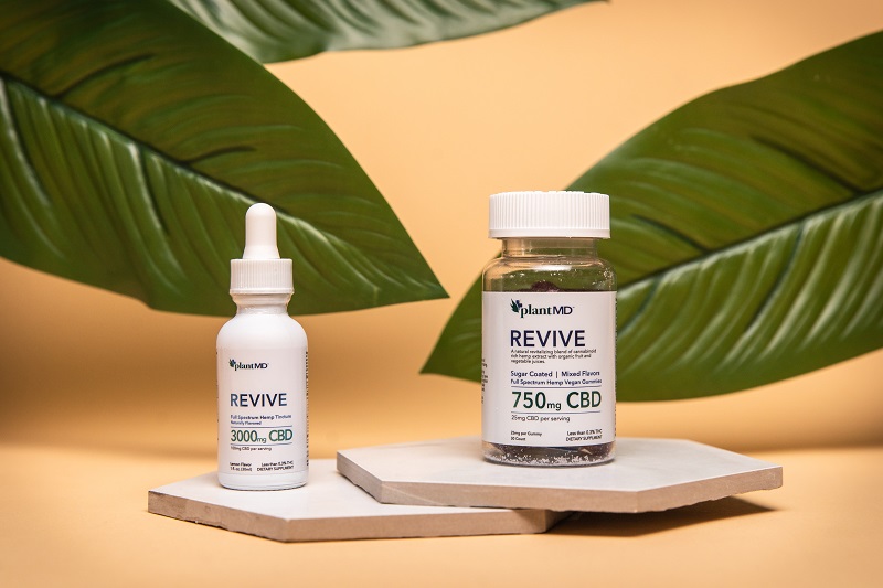 PlantMD Coupon Code PlantMD Revive Gummies and Tincture Sitting on Coasters with Plants in the Background