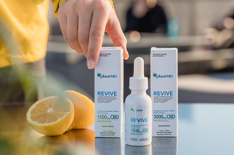 PlantMD Coupon Code PlantMD Revive Products Sitting Next to a Lemon Cut in Half with a Person's Hand Reaching Down to Grab One
