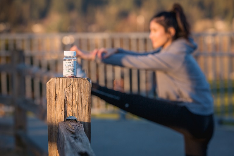 PlantMD Coupon Code Revive Gummies Sitting on a Fence Post with a Woman Stretching Before a Workout Blurry in the Background