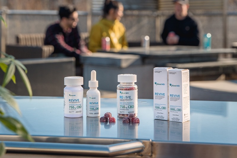 Benefits of PlantMD CBD Plant MD Revive Products Sitting on a Table Outside with People in the Background