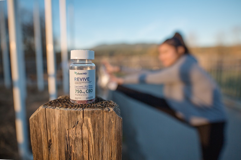 Revive CBD Gummies Price Bottle of CBD Gummies Sitting on a Fence Post with a Woman Stretching in the Background