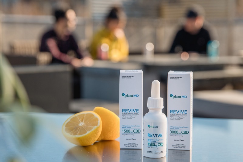 Where to Buy PlantMD CBD Products Lined Up on a Table with People Sitting Around Another Table in the Background