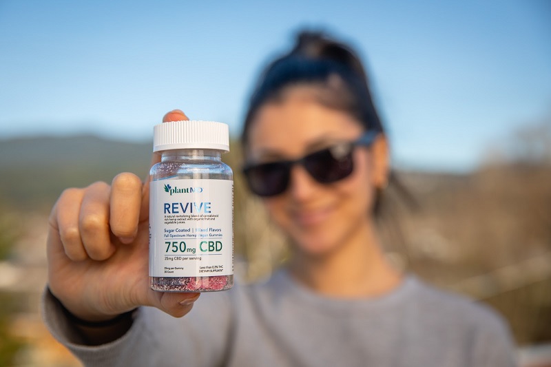 Difference Between CBD Isolate Gummies and Full Spectrum Gummies Woman Holding Up a Bottle of PlantMD Revive Gummies